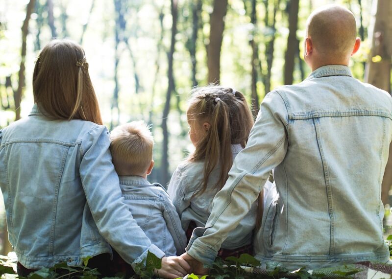 man and woman holding hands together with boy and girl looking at green trees during day